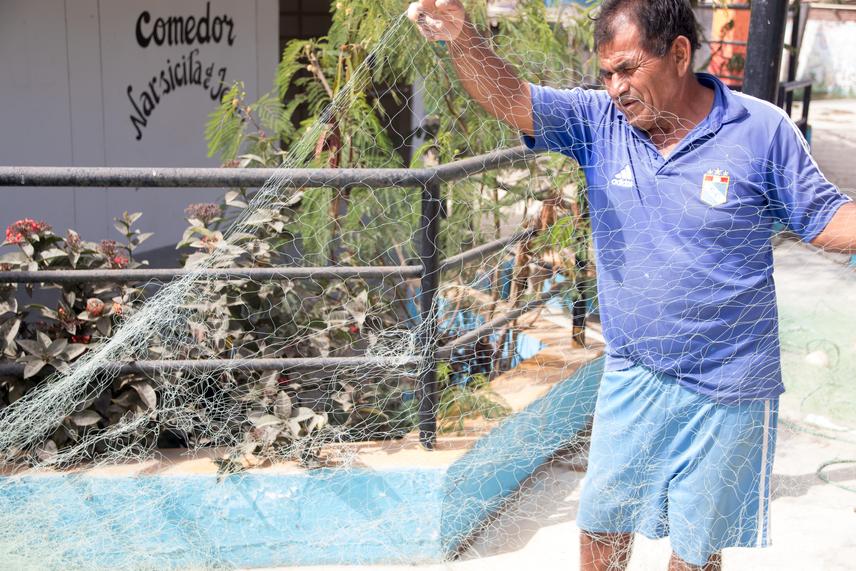 Fisher holding a gillnet with holes caused by whales’ transit and sea lions. (c) Aurora Maguiña Silva