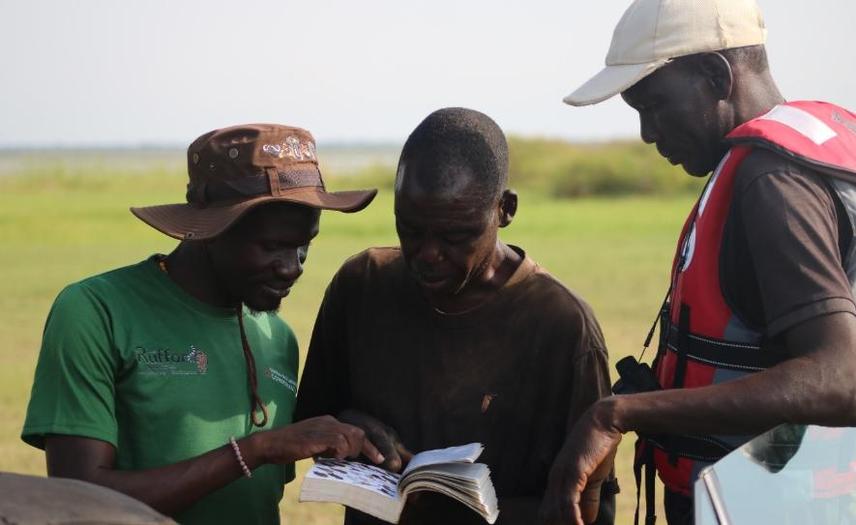 Project Lead, Oreret Erasmus Tukei (in green t-shirt) giving Citizen Scientists (Opio, center and Eraru Dan, right) on field training on how to identify birds using a Bird book © Samuel Onep